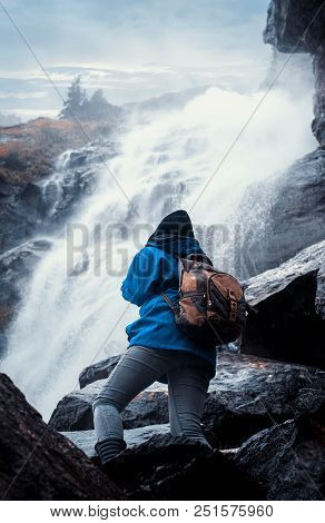 Traveler With A Backpack Climbing On A Mountain Near A Waterfall.