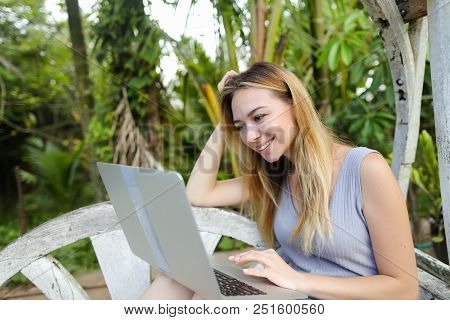 Happy Girl Using Laptop And Sitting In Exotic Garedn With Palms In Background. Concept Of Summer Vac