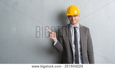 Young redhead man wearing architect outfit and helment very happy pointing with hand and finger to the side