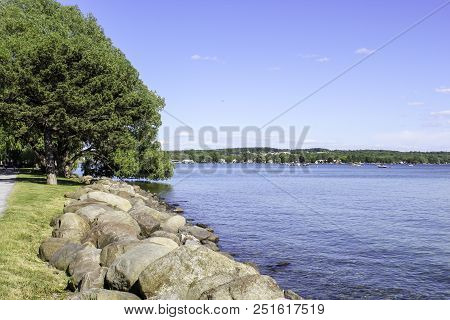 Lakeshore And Horizon On Canandaigua Lake. Calm Blue Water And Rocks Along The Shore At Kershaw Park