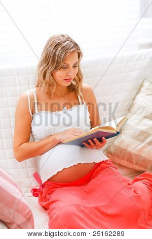 Divan üzerinde oturan ve kitap okumak güzel hamile kadın