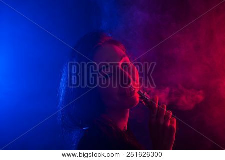 Portrait Of Asian Woman Smoking Vape Or E-cigarette In Neon Light At Black Background