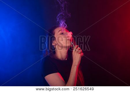 Portrait Of Asian Woman Smoking Vape Or E-cigarette In Neon Light At Black Background