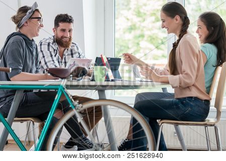 Four proficient freelancers and independent contractors co-working on tablets and laptops, connected to internet at a shared desk behind a commuter bike in a modern work hub