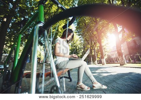 Cute Romantic Girl With Green Bicycle Sitting On Beanch And Working With Laptop In The Sunny Summer 