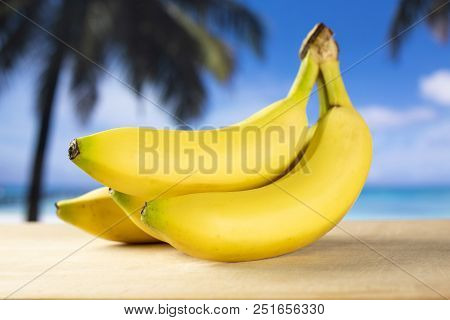 Group Of Three Whole Fresh Yellow Banana One Cluster With Palm Trees On The Beach In Background