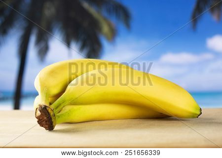 Group Of Four Whole Fresh Yellow Banana One Ripe Cluster With Palm Trees On The Beach In Background