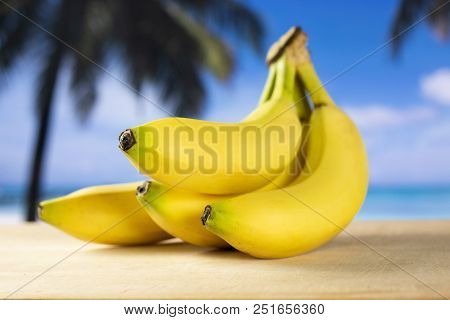Group Of Four Whole Fresh Yellow Banana One Cluster With Palm Trees On The Beach In Background