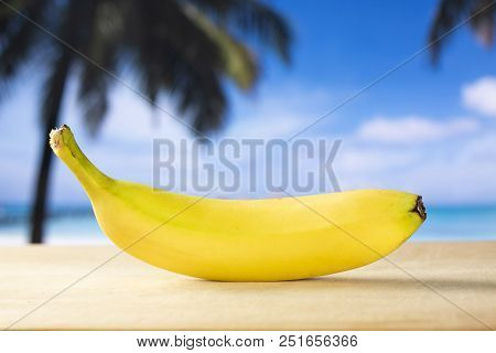 One Whole Fresh Yellow Banana With Palm Trees On The Beach In Background
