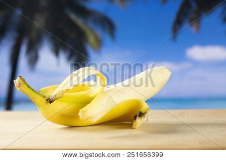One Whole Open Fresh Yellow Banana With Palm Trees On The Beach In Background
