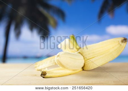 One Whole Fresh Yellow Banana Opened Like A Plane With Palm Trees On The Beach In Background