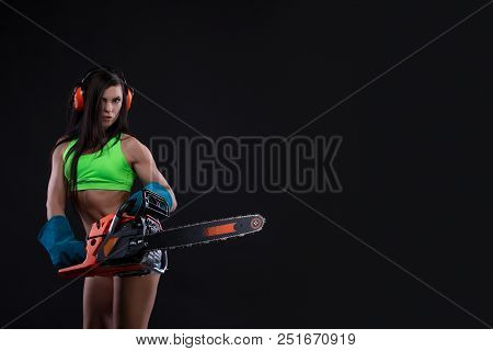Studio Photography Of A Girl With A Chain Saw On Dark Background. Sexy Builder Woman. Copy Space