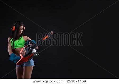 Studio Photography Of A Girl With A Chain Saw On Dark Background. Sexy Builder Woman. Copy Space
