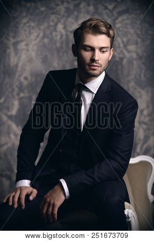 Portrait of a handsome man in an elegant suit sitting in an armchair on a grunge background. Studio shot.
