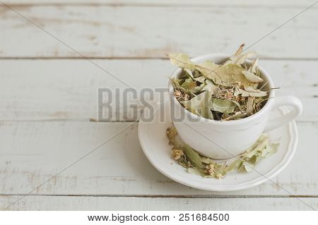 White Cup With Dried Lime Flowers On Wooden Table. Herbal Tea. Healthy Autumn Drink