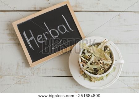 Dried Lime Flowers In A White Tea Cup And Framed Blackboard With Text 