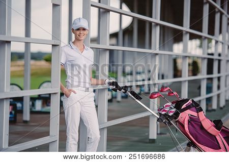 Smiling Female Golf Player In While Polo And Cap With Golf Equipment At Golf Course