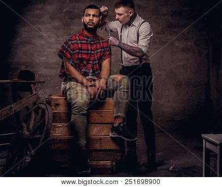 Handsome African American Man Getting A Haircut While Sitting On Wooden Boxes At A Studio. Old-fashi