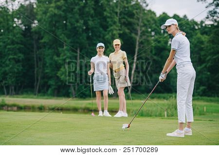 Selective Focus Of Woman In Cap Playing Golf While Friends Standing Near By At Golf Course