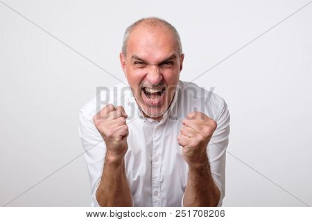 Mature Hispanic Man Is Happy With His Win. He Is Holding His Fists And Shout Wow. Sign Of Victory Is