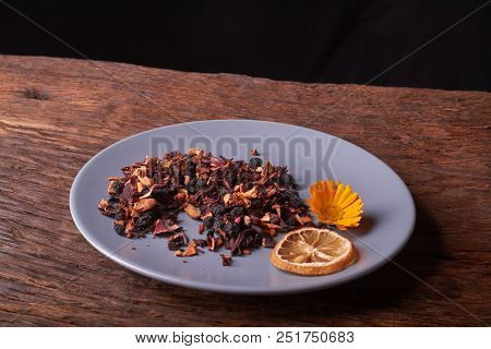 Black Dry Fruit Tea Leaves In Blue Plate On Wooden Table