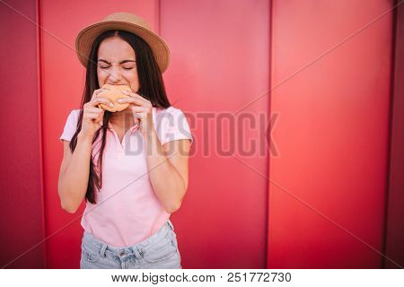 A Picture Of Girl Stands And Bites A Piece Froom Roll. She Holds It With Both Hands. Woman Is Keepin