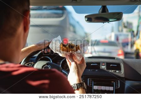 Man Driving Car While Eating Hamburger. Waiting And Standing In Traffic Jam