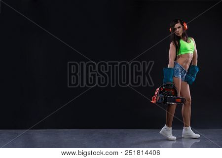 Studio Photography Of A Sexy Girl With A Chain Saw On Dark Background. Copy Space