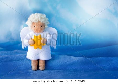 White Felt Christmas Angel With Yellow Star In Hands On Blue Silk Background, Toned.