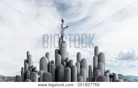 Young Female Doctor With Folder In Hands Satnding On Stone Column