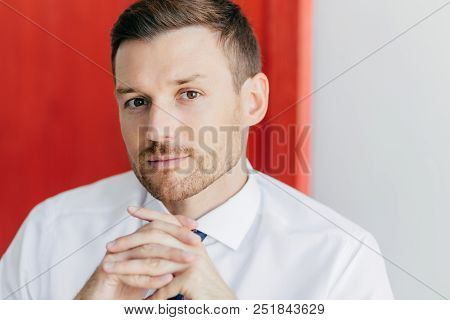 Cropped Image Of Confident Young Male Employee With Bristle, Keeps Hands Pressed Together, Dressed I