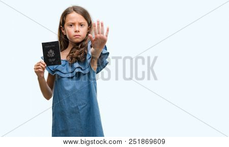 Brunette hispanic girl holding passport of United States of America with open hand doing stop sign with serious and confident expression, defense gesture