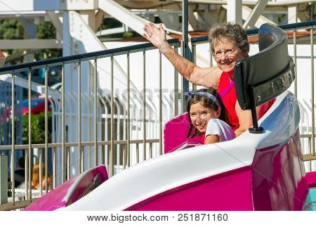 An Elderly Woman Rides On A Tilting, Spinning, Whirling Ride At A Theme Park With Her Young Granddau
