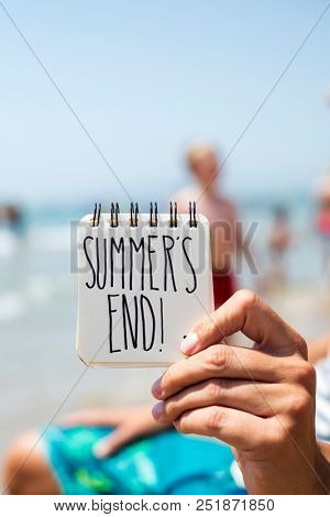 closeup of a young caucasian man on the beach showing a spiral notepad with the text summers end handwritten in it
