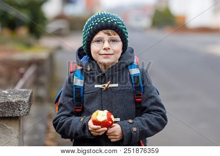 Little Kid Boy With Eye Glasses On The Way To The School And Eating Fresh Apple. Child On A Street. 
