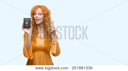 Young redhead woman holding passport of United States of America surprised with an idea or question pointing finger with happy face, number one