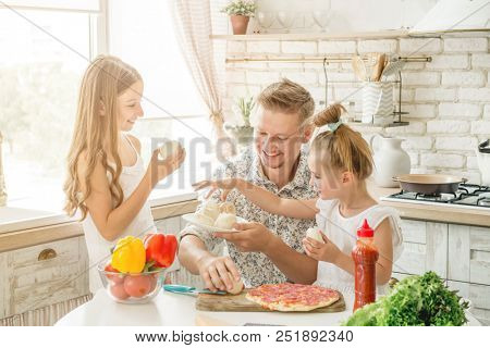 Dad with two small daughters preparing pizza with mushrooms in the kitchen