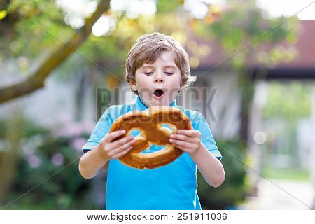 Adorable Little Kid Boy Eating Huge Big Bavarian German Pretzel. Happy Blond Child Enjoying Tasteful