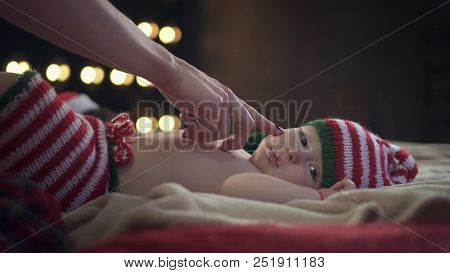 Female Playing With Baby Boy Who Is Lying On Bed In Striped Cap, Softly Touching His Nose And The Ba