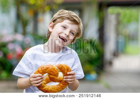 Adorable Little Kid Boy Eating Huge Big Bavarian German Pretzel. Happy Blond Child Enjoying Tasteful