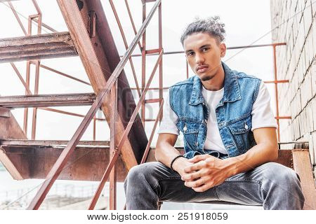 Stylish Mixed Race Man Sittng On Stairs And Looking At Camera At Urban Street