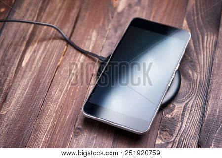 Mobile Phone Lies On A Wireless Charger On A Wooden Brown Background