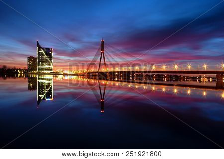 Sunset On The River Daugava Against The Background Of A Cable Bridge And A Skyscraper With Reflectio