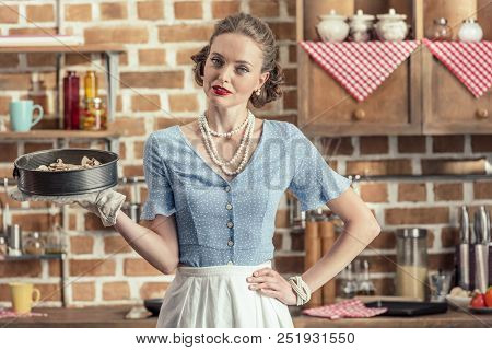 Beautiful Adult Housewife Holding Baking Trey And Looking At Camera At Kitchen