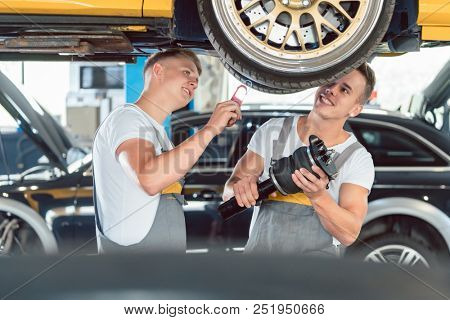 Two skilled auto mechanics analyzing together the rims of a lifted car while working in a modern automobile repair shop
