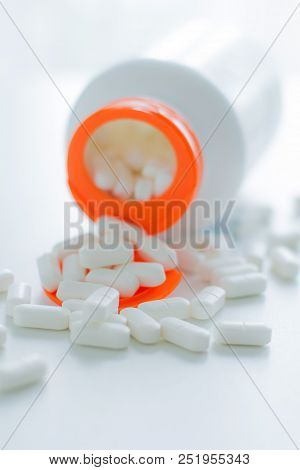 White Tablets Spilling Out Of Plastic White Bottle With A Tablet