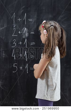 Schoolgirl Standing In Front Of A Blackboard, Solving Math Equations, Practising Summation. Focus On