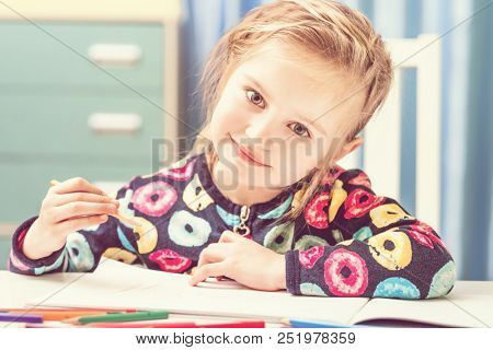 Charming blonde little girl with beauriful eyes draws with pencils and looks at camera