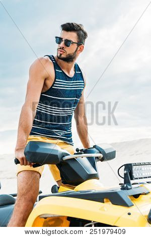 Handsome Young Man Standing On All-terrain Vehicle And Looking Away