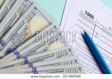 1065 Tax Form Lies Near Hundred Dollar Bills And Blue Pen On A Light Blue Background. Us Return For 